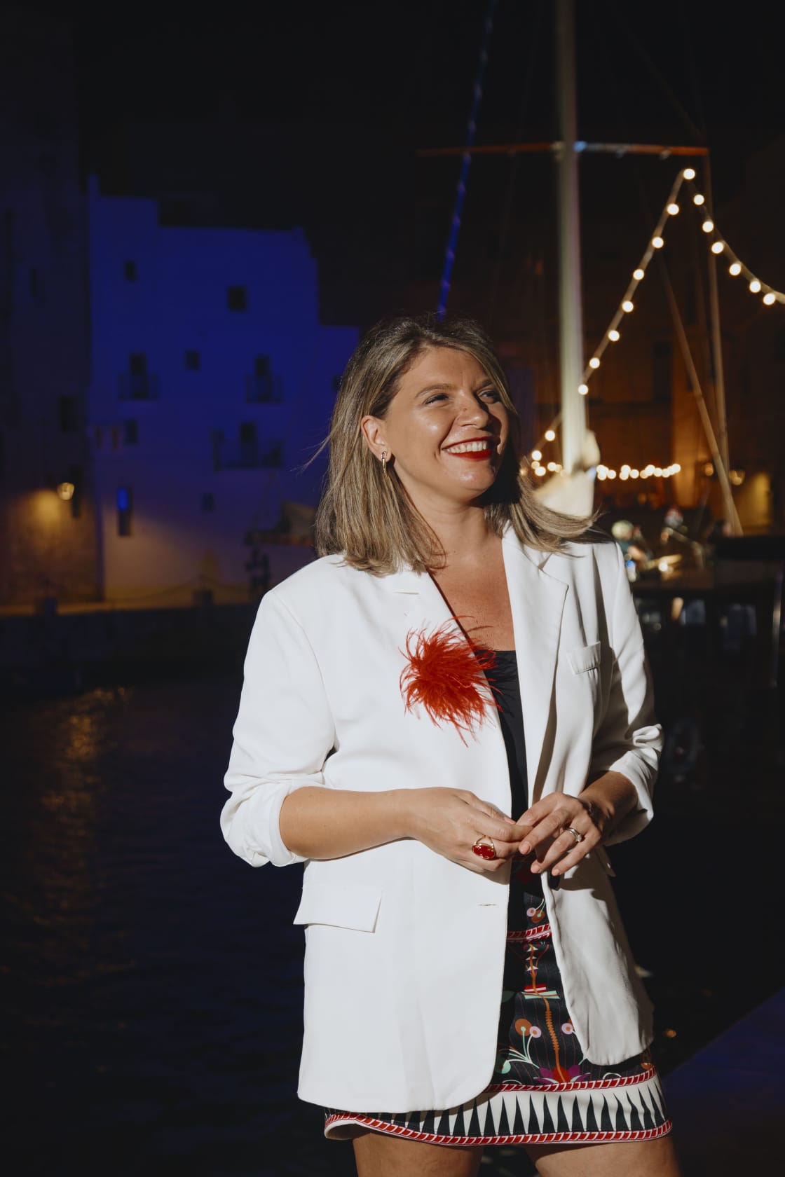 Laura Rubino sorridente di sera al porto, tra luci calde e barche a vela
